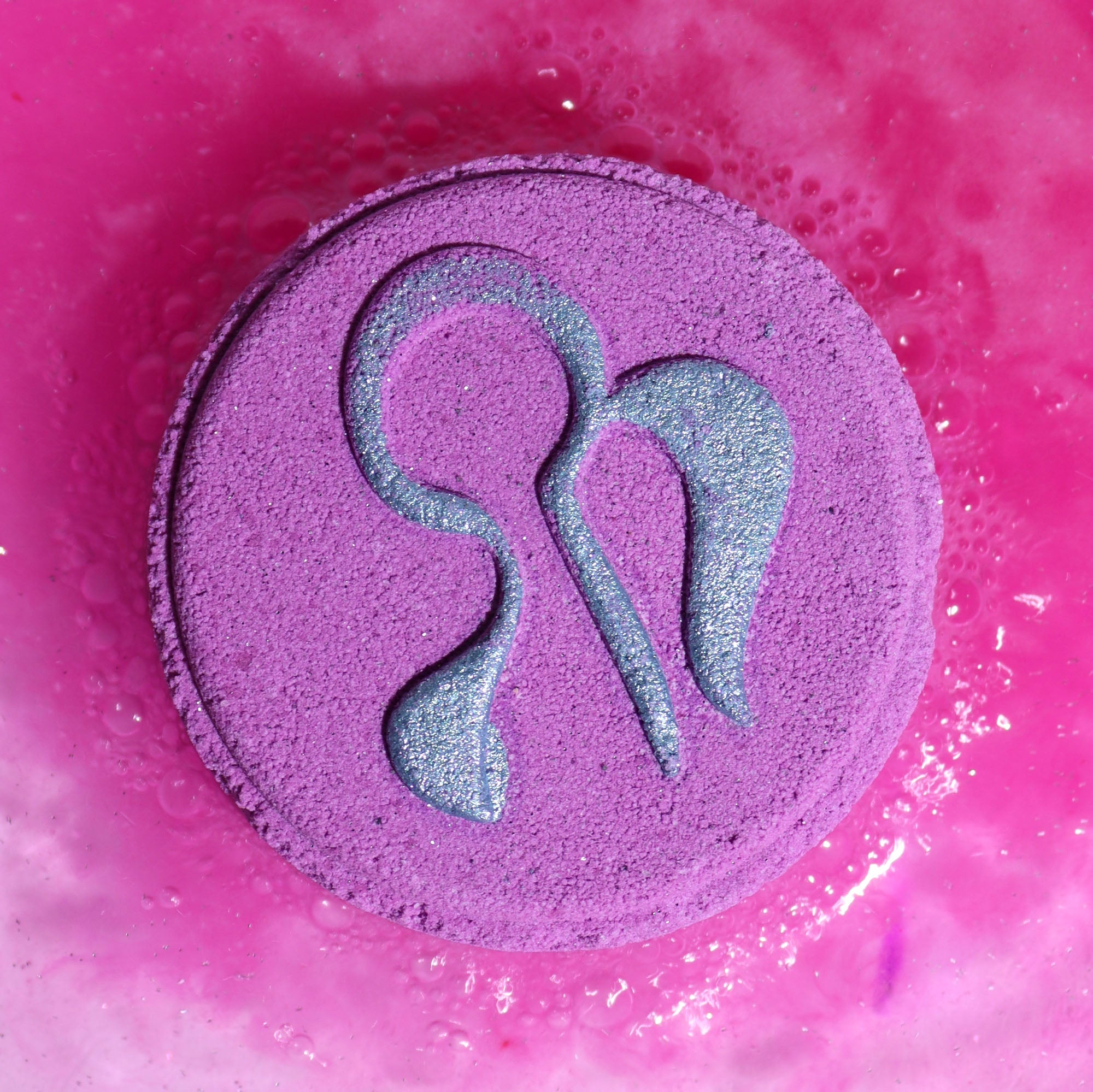Close-up of Virgo Zodiac symbol on a circular Bath Bomb fizzing in bathwater, infused with floral and warm woody scents.
