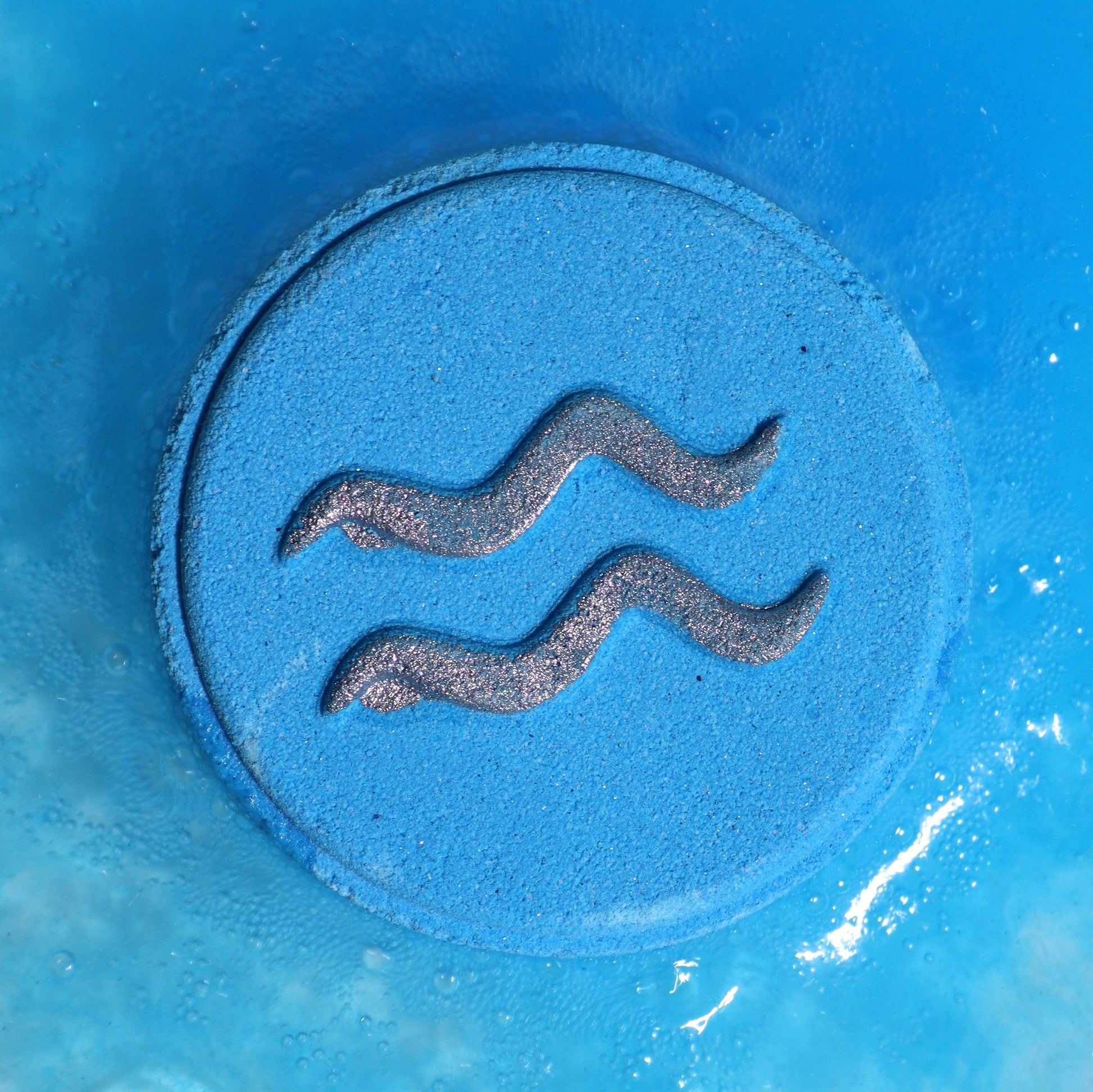 Close-up of Aquarius bath bomb fizzing with shades of blue and soothing fragrance,a silver symbol of water on a circular bath bomb