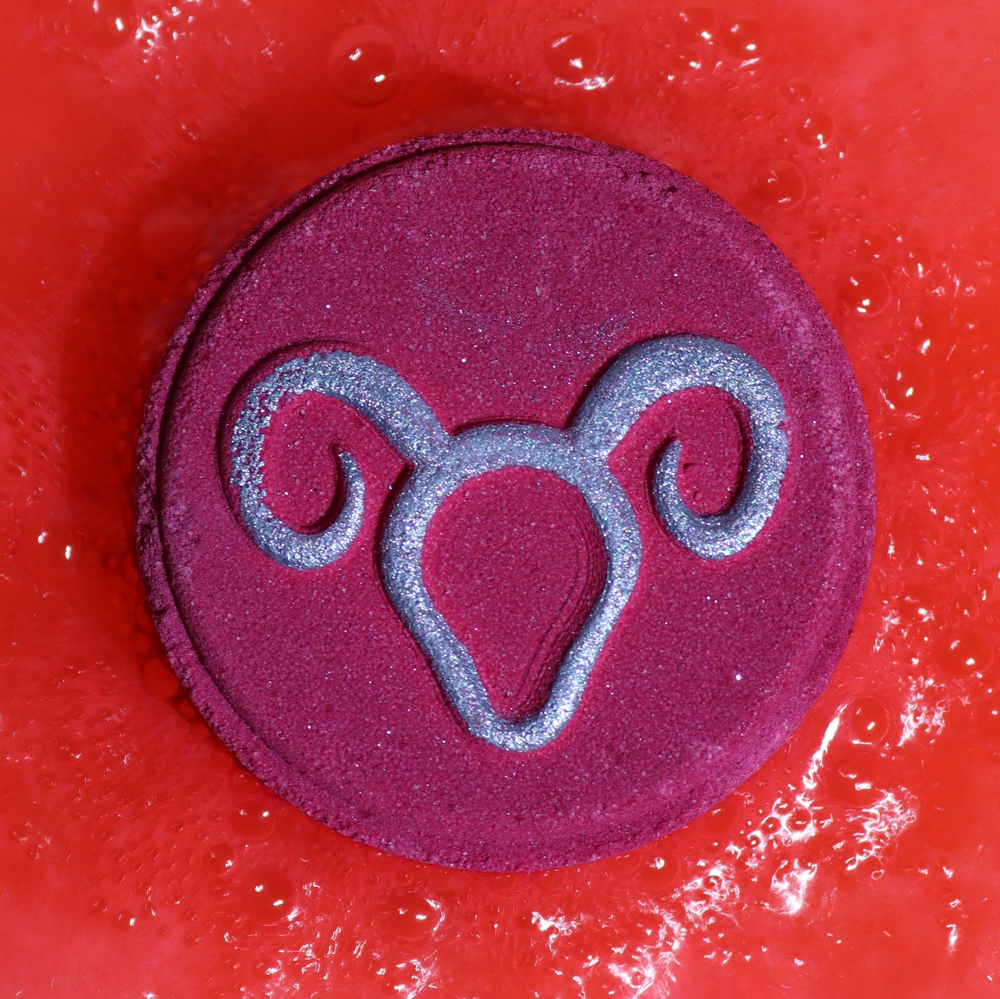 Close-up of Aries bath bomb fizzing in water with fresh, invigorating fragrance, with silver symbol on a circular bath bomb
