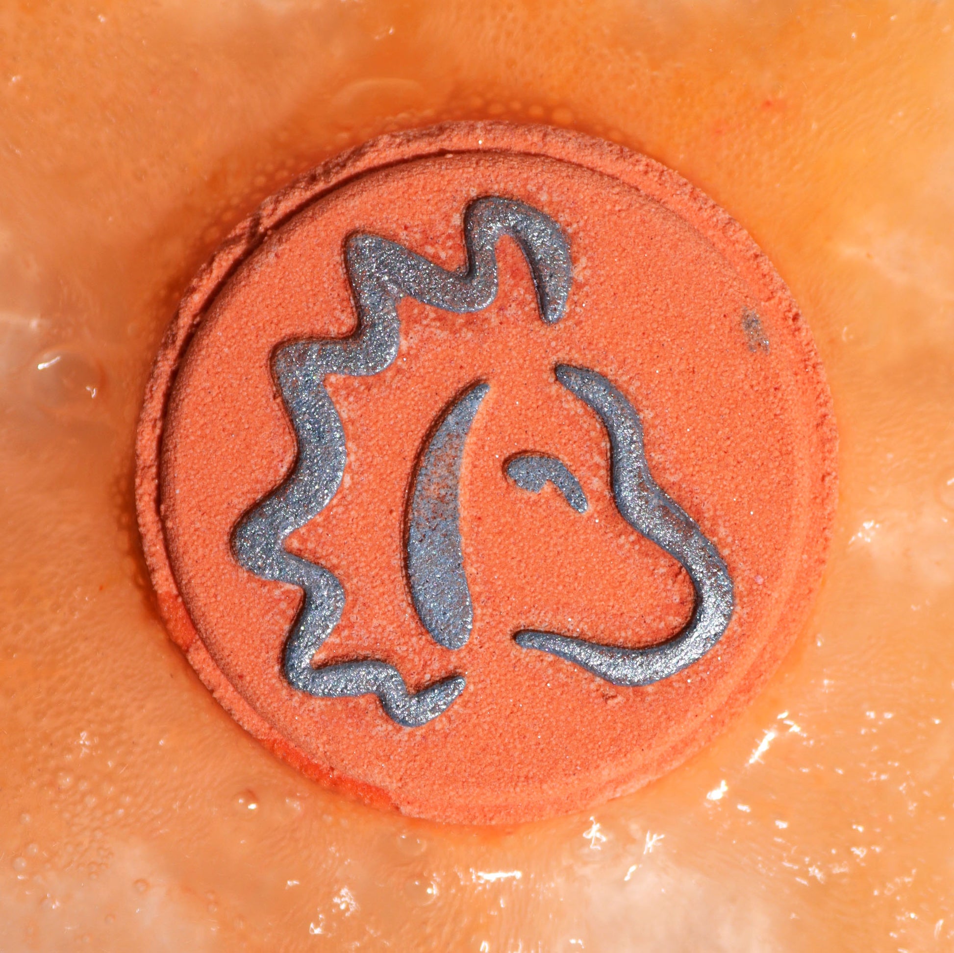 Close-up of Leo bath bomb fizzing in golden water with vibrant citrus fragrance