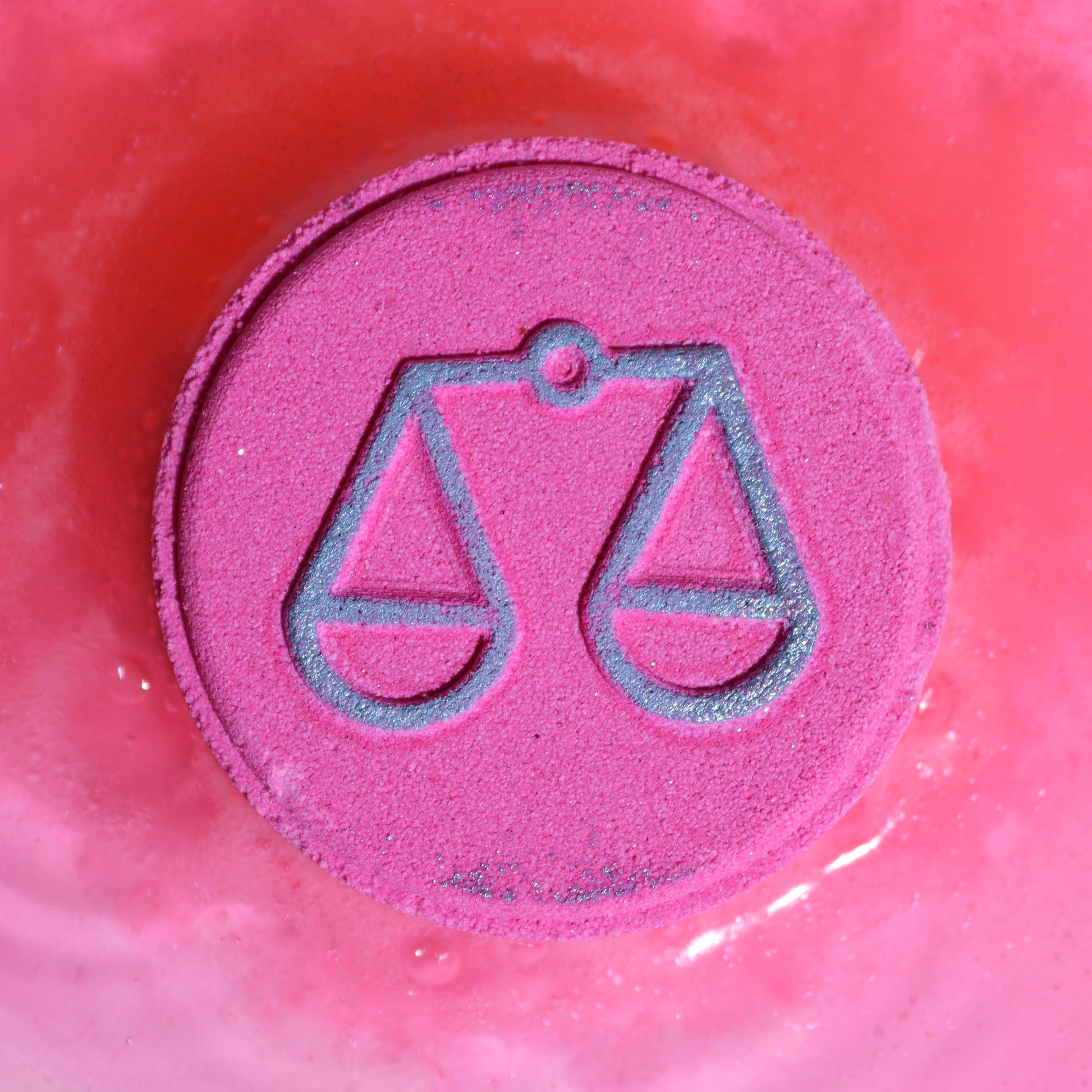 Close-up of Libra bath bomb fizzing with floral fragrance, with Libra zodiac symbol on a pink circular bath bomb