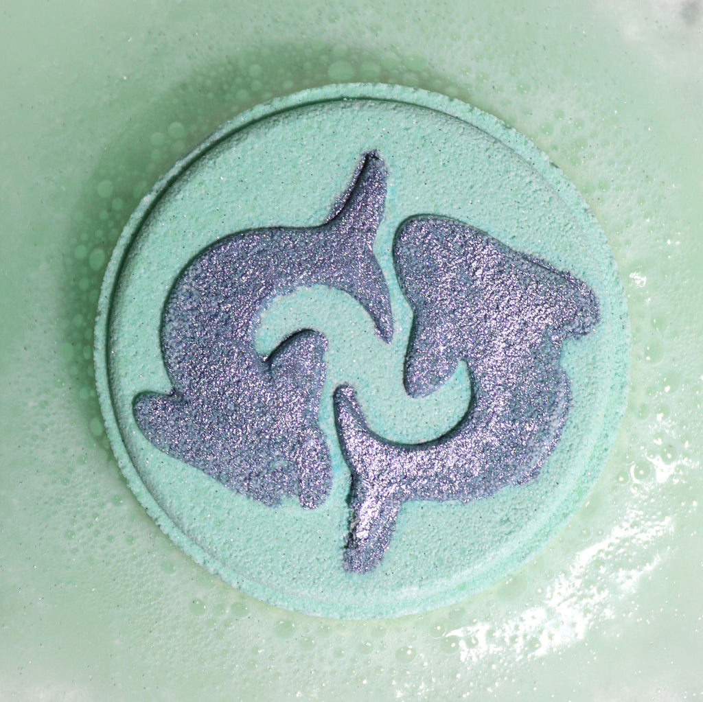 Close-up of Pisces bath bomb fizzing with soft, dreamy colours and gentle floral fragrance, with a dolphin design on a light green circular bath bomb